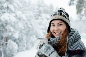 Woman in winter clothes outside holding a mug and smiling