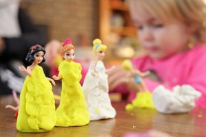 Little girrl putting play-dough around dolls