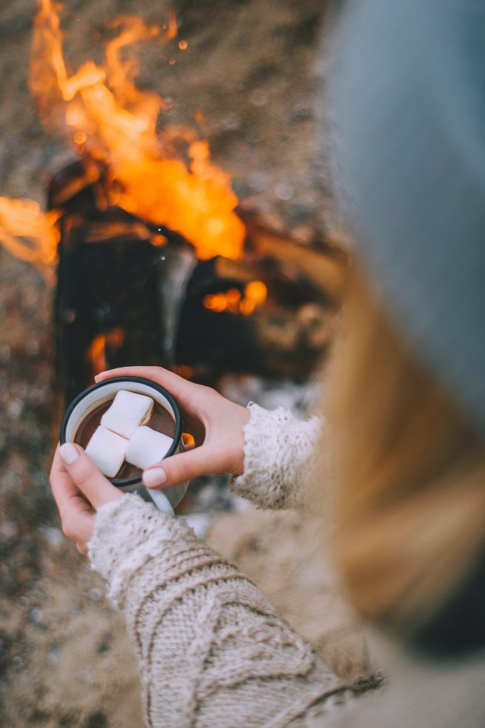 Woman sitting by an outdoor fire with hot chocolate